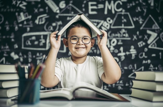 A boy with glasses studied and put a book on his head in the classroom.